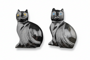 Two polished black cat-shaped carving s with carved fur details and one featuring yellow-gold and the other blue inlaid eyes, displayed side by side on a white background.