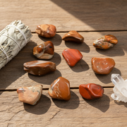 Collection of tumbled stones and a smudge stick on a wooden surface