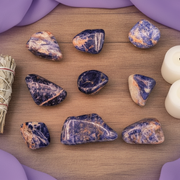Set of orange and blue stones on a wooden surface with a bundle of sage and candles.