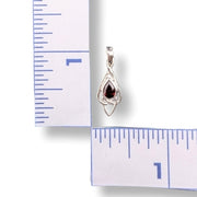 Silver pendant with a red gemstone next to a ruler for scale on a white background