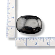 Black tourmaline palm stone with a ruler for scale on a white background