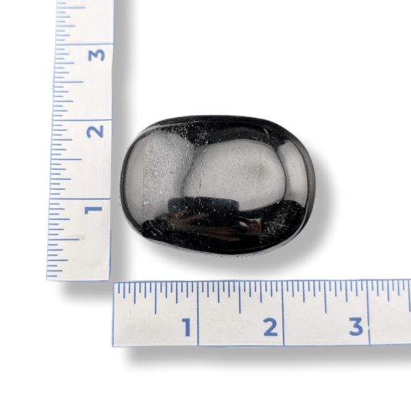 Black tourmaline palm stone with a ruler for scale on a white background
