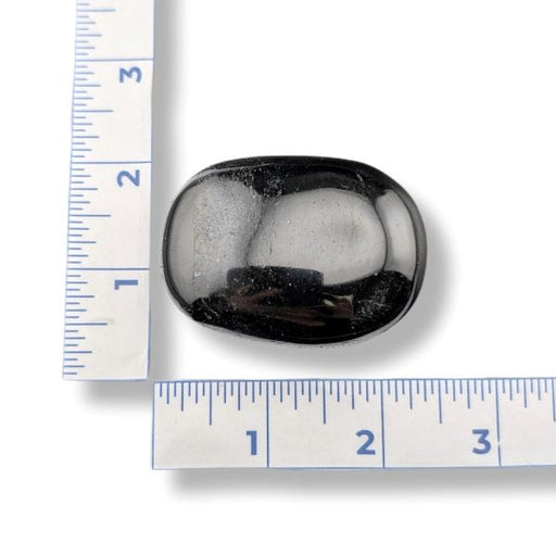 Black tourmaline palm stone with a ruler for scale on a white background