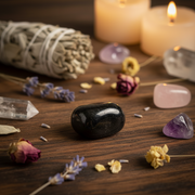 Black stone, crystals, and dried flowers on a wooden surface with candles in the background.