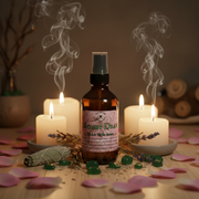 A bottle of Earthworks Enchantments Room Spray Money Draw, stands on a wooden surface surrounded by lit white candles, rose petals, green stones, dried lavender, and a smudge bundle, with smoke rising in the background.