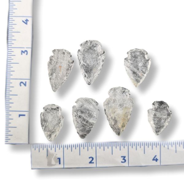 Six small pointed stone arrowheads arranged on a white background with a measuring ruler along the left and bottom edges for scale.