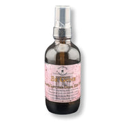 A dark amber glass spray bottle with a silver pump dispenser and a pink label reading 'Be Gone'  shown on a white background with a soft shadow.
