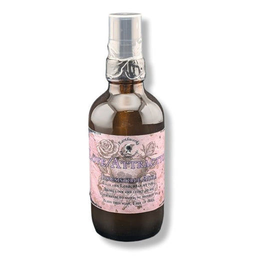 An amber glass spray bottle with a pink and white label reading 'Love/Attraction'  topped with a clear plastic spray cap, shown on a white background.