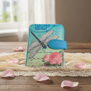 Decorative wallet with dragonfly and floral design on a wooden surface with pink petals.