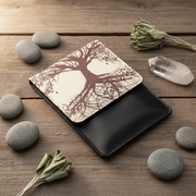 Black crossbody bag with tree design on a wooden surface with stones and plants