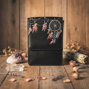 Black leather bag with dreamcatcher design on a wooden surface with crystals and herbs.