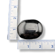 Black stone with a reflective surface next to a ruler on a white background