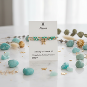 A Pisces zodiac-themed bracelet display card on a white marble surface, surrounded by light blue stones and gold accents. The bracelet features a gold triple-C chain, turquoise beads, and a small gold cross charm.
