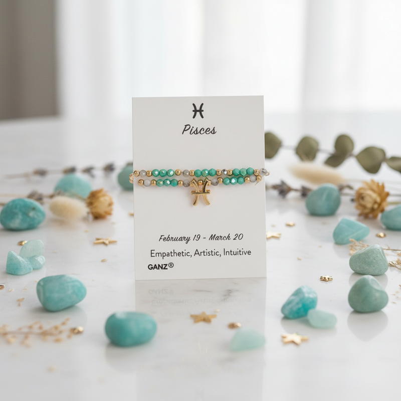 A Pisces zodiac-themed bracelet display card on a white marble surface, surrounded by light blue stones and gold accents. The bracelet features a gold triple-C chain, turquoise beads, and a small gold cross charm.
