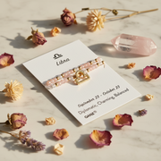 A Libra-themed beaded bracelet, displayed on a white card labeled 'Libra' with decorative dried flowers and crystals on a marble surface.
