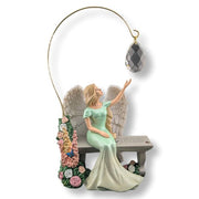 Decorative angel figurine with wings, sitting on a bench holding a crystal ball, on a white background.
