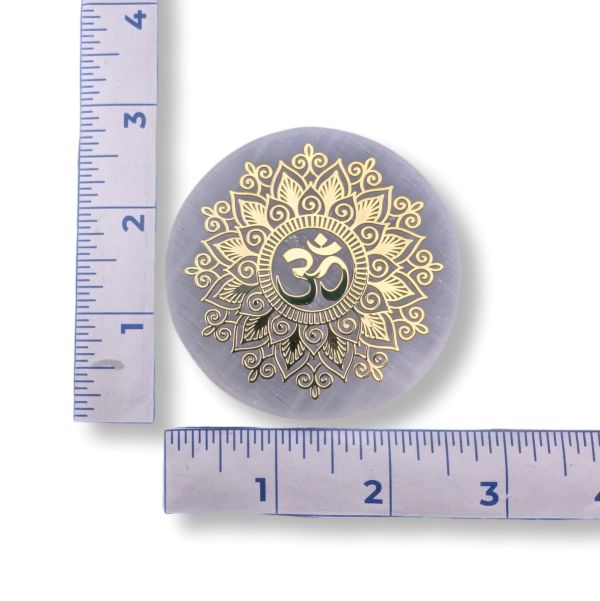 Round selenite stone with gold mandala design and Om symbol, measured against a ruler on a white background