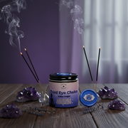 Third Eye Chakra candle with incense sticks and amethyst crystals on a wooden surface.
