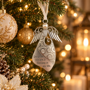 A silver metal angel ornament with engraved floral patterns and the message 'Daughter, you are a blessing in my life,' hanging on a decorated Christmas tree with warm bokeh lights in the background.