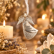 An ornate silver angel ornament with a white pearl and engraved text reading 'A friend like you is precious and few,' hanging in a warm, softly blurred setting with candles, dried flowers, and crystals.
