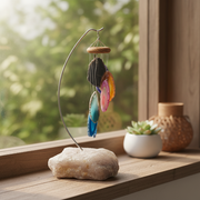 A hanging crystal wind chime with colorful polished stone slices on a curved metal stand, placed on a wooden windowsill next to a small potted succulent and a woven decorative jar.