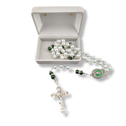 Pearl and green stone rosary with a silver cross in an open gray jewelry box on a white background.