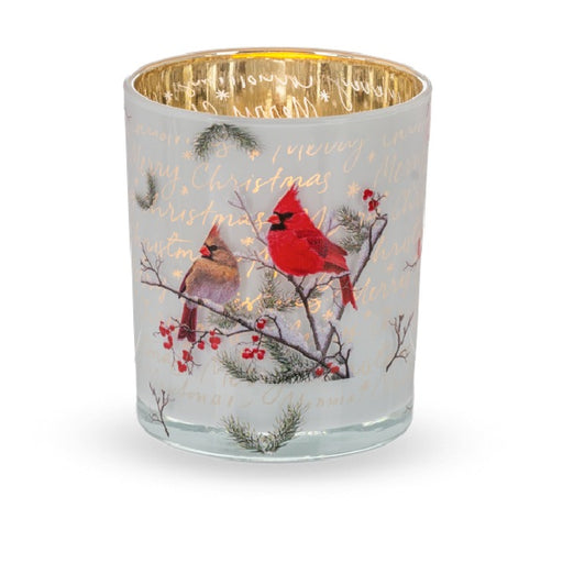 A clear glass jar candle with a metallic gold interior and a festive Christmas design featuring red cardinals on pine branches with red berries and gold cursive text, set against a plain white background.