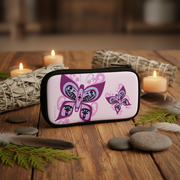 A rectangular zip pouch with a black border and a light pink printed design featuring two purple butterflies, styled on a wooden surface with candles, smudge bundles, stones, and feathers.