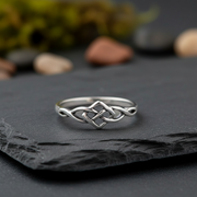 Silver Celtic knot ring on a dark stone surface with blurred natural background