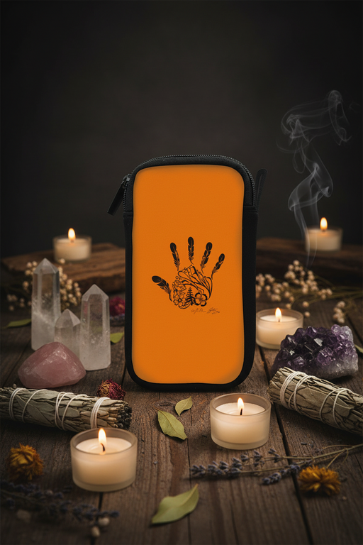 An orange zippered pouch with a black handprint graphic featuring a brain illustration, displayed on a rustic wooden table surrounded by lit candles, crystals, and dried herbs.