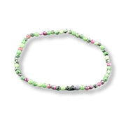 A beaded stretch bracelet made of small round gemstone beads in shades of green, pink, and black, arranged in an oval shape on a white background.