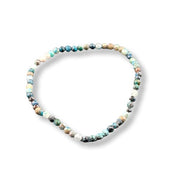 A beaded stretch bracelet made of small, polished round beads in a marbled mix of turquoise blue, green, white, brown, and black, displayed on a clean white background.