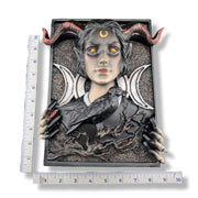 A gothic fantasy wall plaque featuring a horned woman with glowing orange eyes, black horns, white triple moons, skeletal hands, a raven, and a barren tree, shown with measurement rulers on a white background.