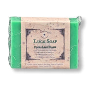 A wrapped bar of bright green soap with a paper label reading 'Luck Soap' and 'Four Leaf Flame,' photographed on a plain white background.