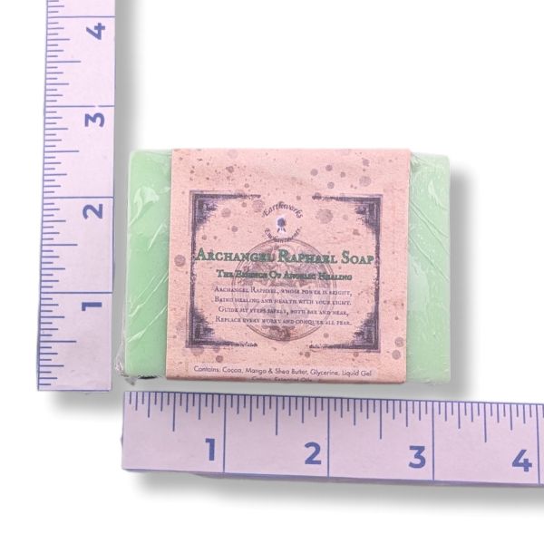 A rectangular bar of soap wrapped in clear plastic with a dusty pink paper label reading 'Archangels Raphael Soap,' shown on a white background with purple rulers measuring its width and height.