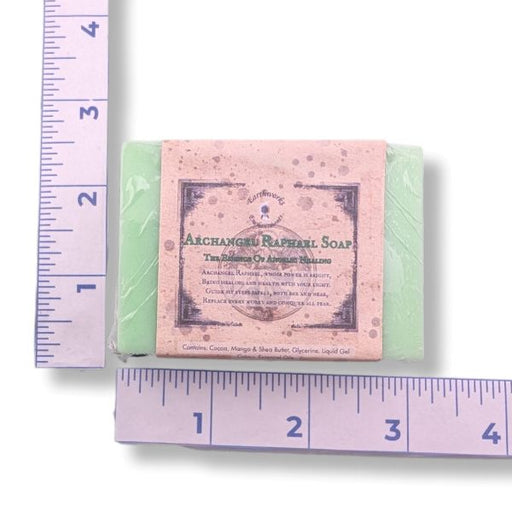 A rectangular bar of soap wrapped in clear plastic with a dusty pink paper label reading 'Archangels Raphael Soap,' shown on a white background with purple rulers measuring its width and height.