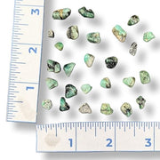 Green mineral stones on a white background with a ruler for scale.