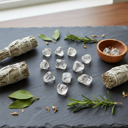 Clear crystals on a dark surface with sage bundles and green leaves