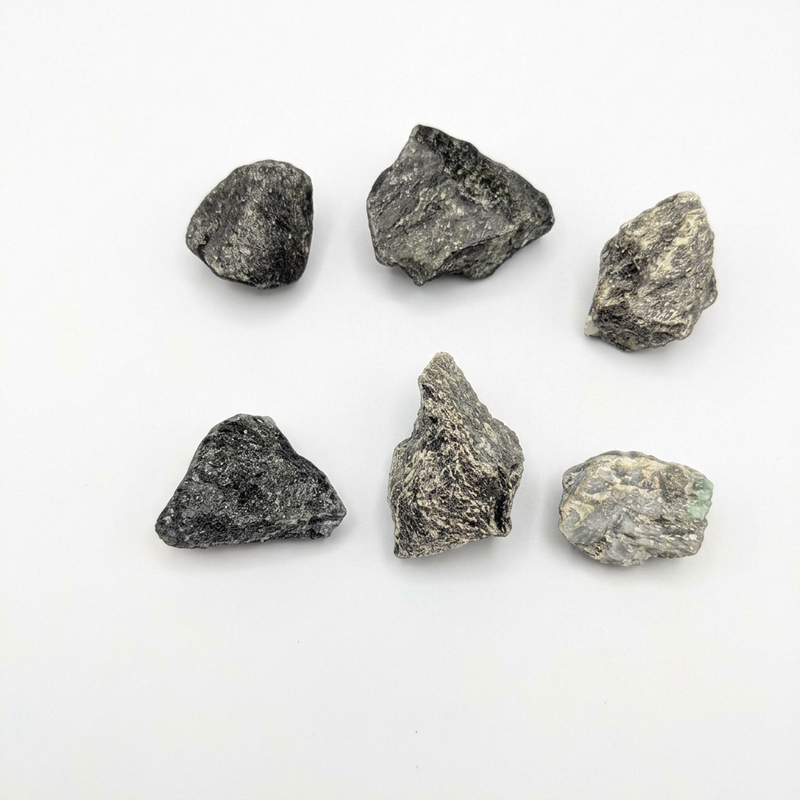 Six rough, unpolished dark gray and black stones arranged in two rows on a plain white background.
