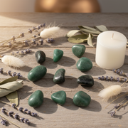 Green stones on a sunlight table with a candle and herbs around them.