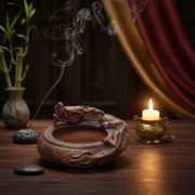 Decorative incense burner with smoking sticks, a candle, and a bamboo plant on a wooden surface.