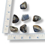 A collection of blue water sapphire tumbled stones of various sizes, displayed in front of a blue measuring tape for scale.