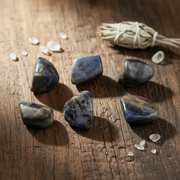 Blue water sapphire in a spiritual setting on a wooden table with sage and other accent crystals