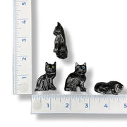 Four black cat figurines of different sizes next to a ruler on a white background