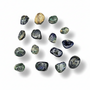 A group of polished tumbled gemstones in dark blue, green, and one natural gold-colored stone, arranged on a white background with soft drop shadows.