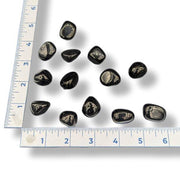A collection of tumbled jet stones of varying sizes placed on a measuring tape to show scale.