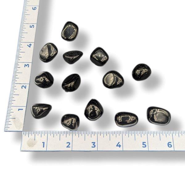 A collection of tumbled jet stones of varying sizes placed on a measuring tape to show scale.