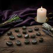 Candle, lavender, and stones on a wooden surface with a dark fabric background