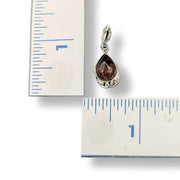 Teardrop-shaped pendant with embedded gemstone next to a ruler for scale