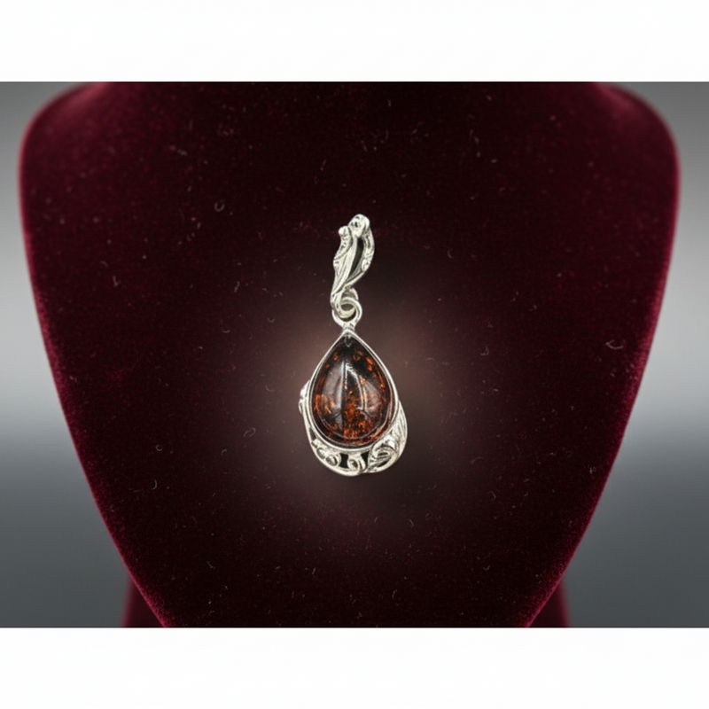 Silver pendant with a teardrop-shaped gemstone on a dark red velvet stand.